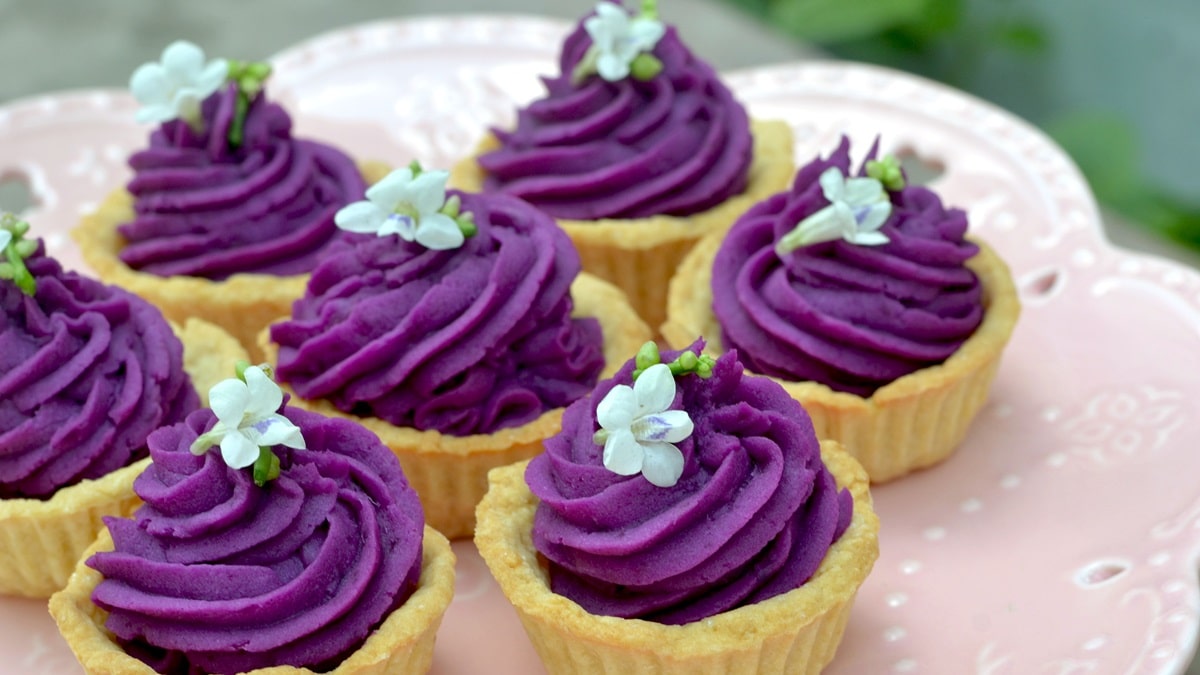 Kuvassa Okinawan violetista bataatista tehtyjä leivoksia, joiden päällä on valkoinen kukka.