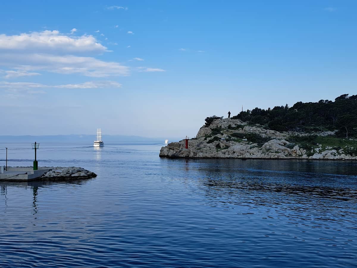 Kroatian risteilyn merimaisemaa, horisontissa purjevene ja etualalla kivikkoinen saari.