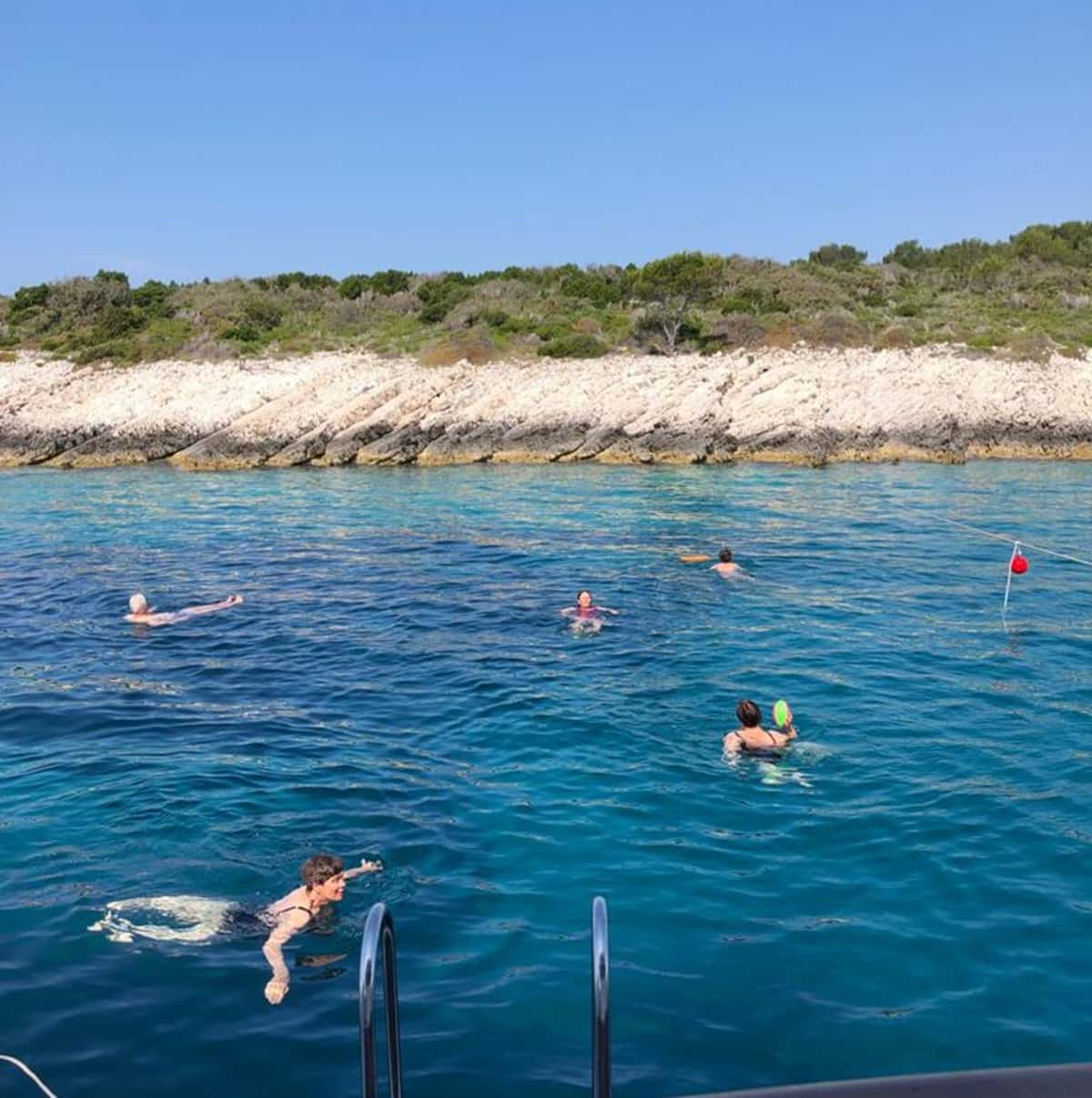 Kroatian risteilyllä uimareita meressä, taustalla saari.