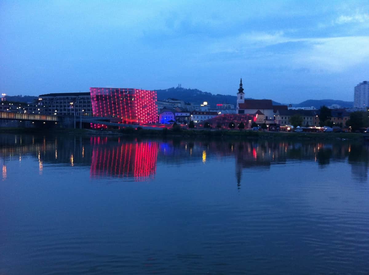 Tonavan varrella sijaitseva Linzin kaupunki ilta-aikaan, kaupungin valot heijastuvat etualalla olevaan veteen. 