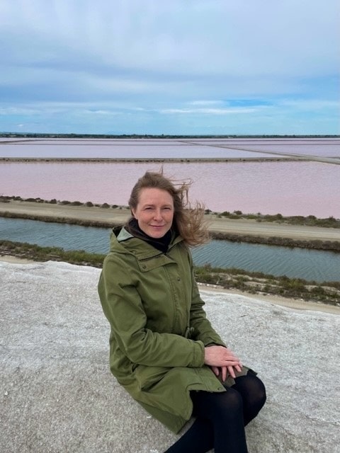 Nainen istuu kivimuurilla, taustallaan vaaleanpunaiset suola-altaat