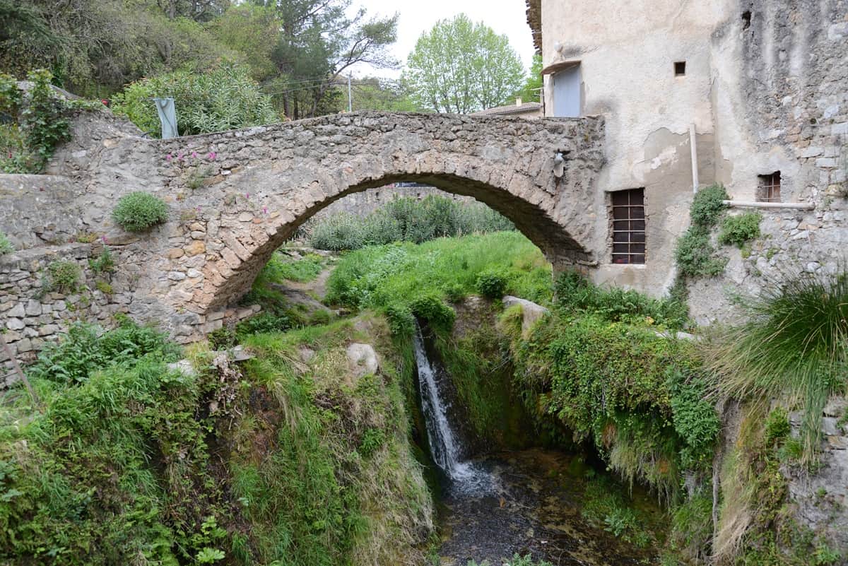 Saint-Guilhem-le-Désertin kylässä vanha pieni kivisilta, jonka alla pieni puro sekä vihreää kasvillisuutta. 
