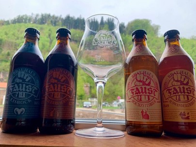 Neljä saksalaista olutpulloa, joiden keskelle maistelulasi. Taustalla ikkuna, jonka takaa näkyy vehreää metsäistä maisemaa. 